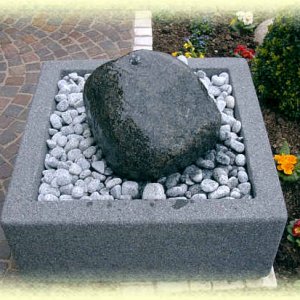 Dunkler       Granit- Quellstein auf hellgrauem Zierkies in Basalt-Becken (Größe       80/80/35 cm)